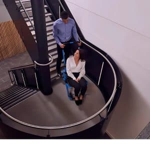 A bloke assists a woman using stair climbers enhance accessibility on a modern staircase.