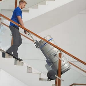 A man wheels a keg up stairs using a hand trolley. Hand trolley safety precautions are vital to avoid injury.