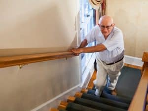 Senior man without home stair lift carefully walking upstairs with support from handrail