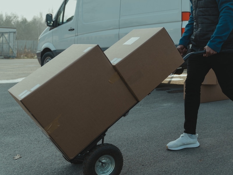 Worker transporting boxes with a heavy duty hand trolley near a delivery van.