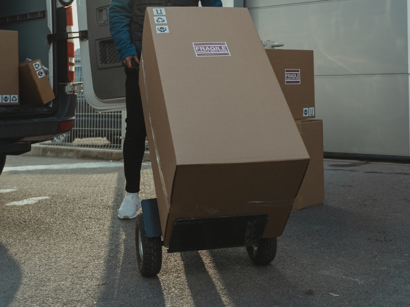 stair climber trolley hire: courier using stair-climbing trolley moves large fragile box from delivery van.