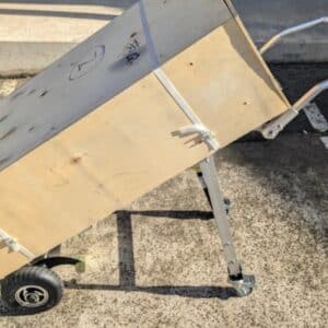 Close-up of heavy crate fixed to stair-climbing trolley, showing straps and adjustable support legs.