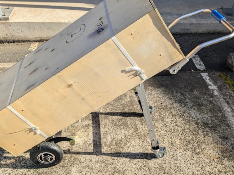 Close-up of heavy crate fixed to stair-climbing trolley, showing straps and adjustable support legs.