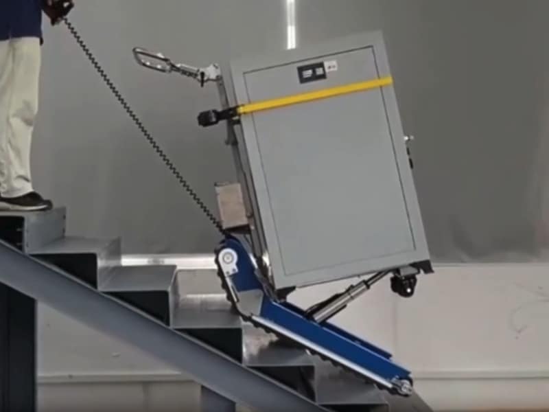 Stair climber rental moving a heavy safe on tracks down metal stairs, operator guiding with remote lead