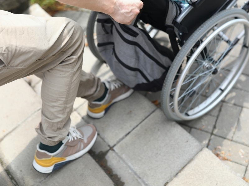 A person assisting a wheelchair user up outdoor steps, highlighting the need for safer stair climbing solutions for accessibility.